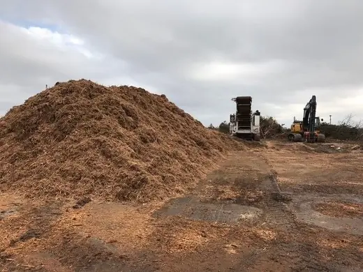 Wood chip pile beside a grinder and excavator on a Countryside land clearing job