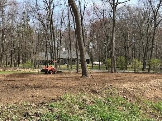 Tractor clearing heavy underbrush at the wooded edge of a residential property